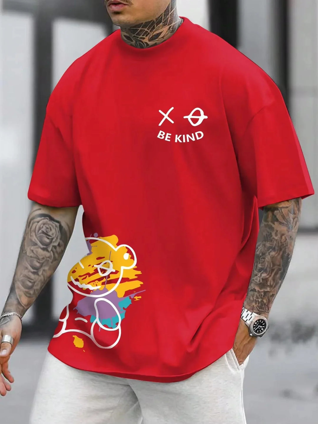 Man wearing red oversized T-shirt with colorful bear and white text 'BE KIND' on chest