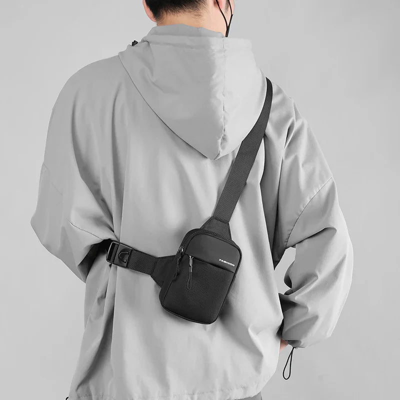 Person wearing light gray hooded jacket with black crossbody travel bag against gray background