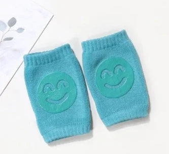 Pair of turquoise knitted knee pads with smiling face design on a white surface