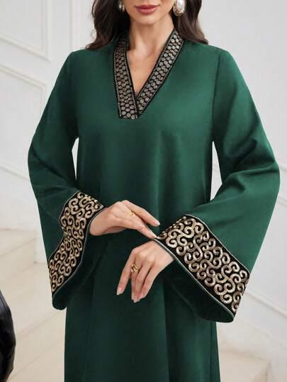 Woman wearing dark green dress with black and gold embroidered V-neck and wide sleeves