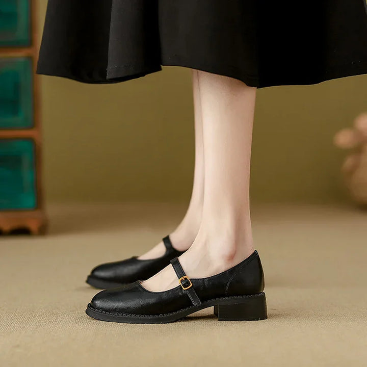 Black Mary Jane shoes with buckle strap worn with black skirt on beige floor
