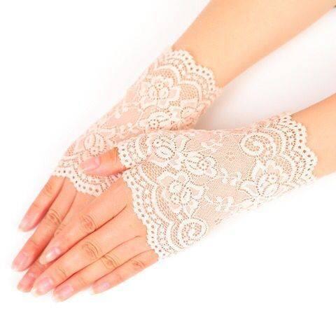 Hands wearing delicate beige lace fingerless gloves with floral patterns on a white background