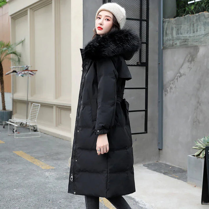 Woman wearing long black puffer coat with large fur hood and knit hat in urban setting