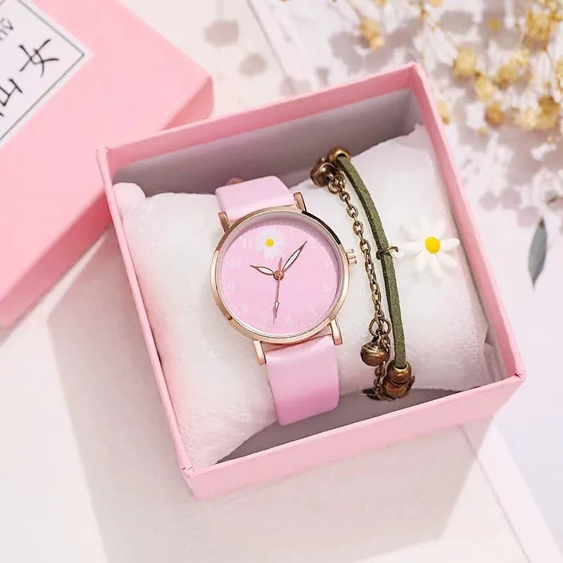 Pink wristwatch with daisy detail and green charm bracelet in pink gift box on white cushion