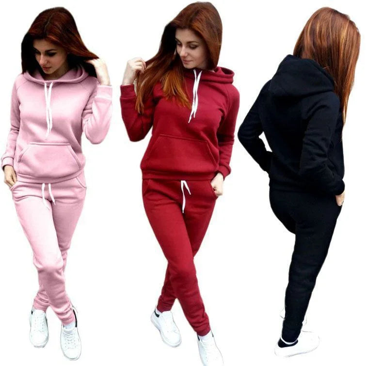 Woman modeling pink, red, and black hooded jogger sets with white sneakers on white background
