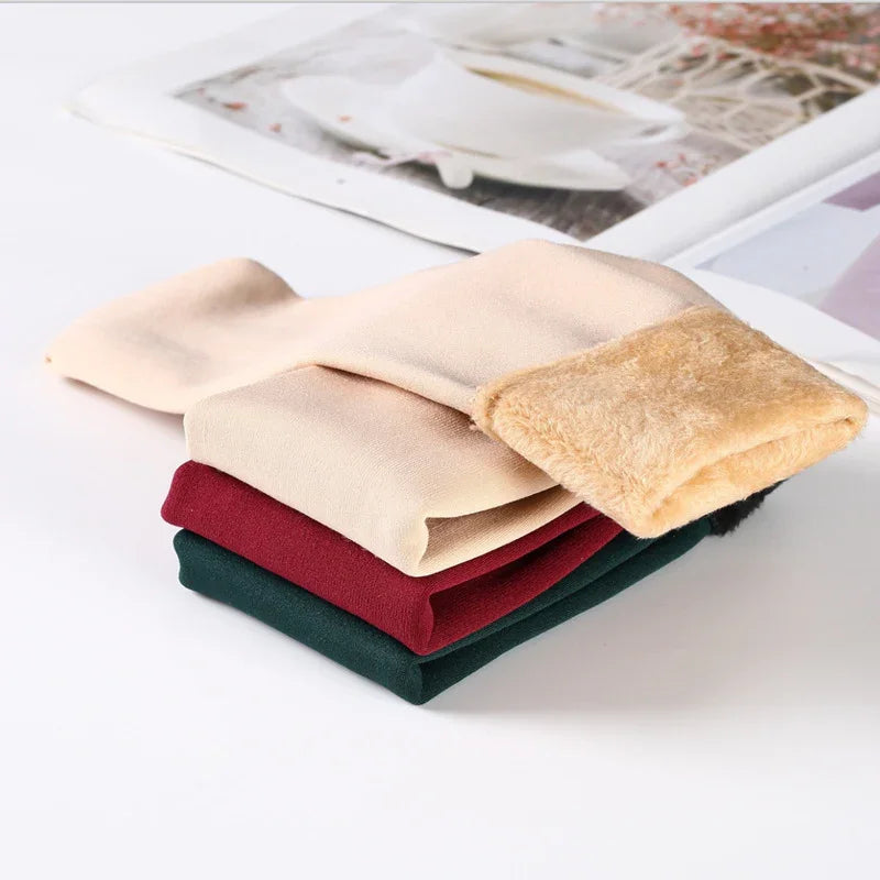Stack of folded warm fleece-lined leggings in beige, red, and dark green on white surface