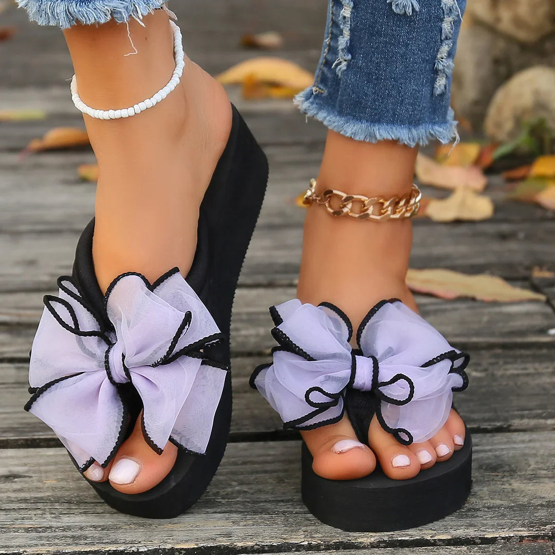 Women's black platform flip-flops with large white bows and black trim on wooden deck