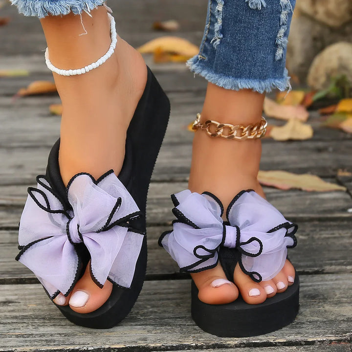 Women's black platform flip-flops with large white bows and black trim on wooden deck