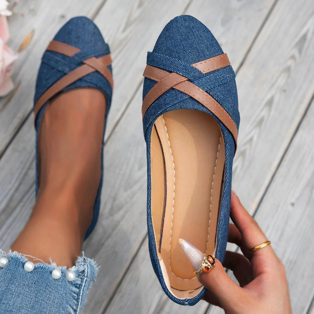 Woman holding and wearing stylish blue denim ballet flats with brown leather straps on wooden floor