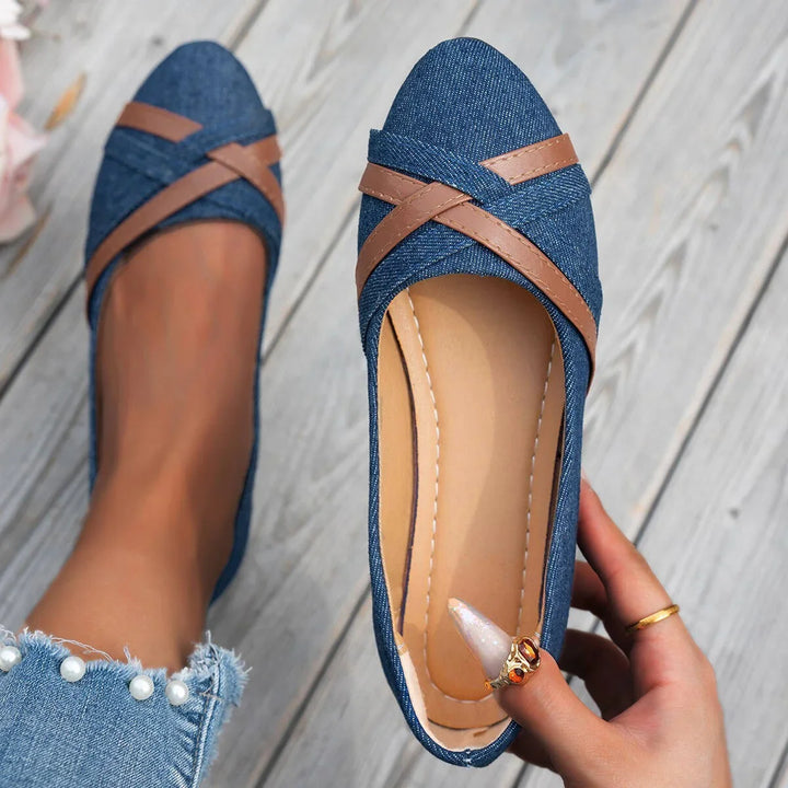 Woman holding and wearing stylish blue denim ballet flats with brown leather straps on wooden floor