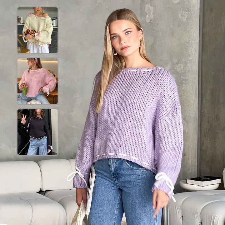 woman wearing chunky knit lavender sweater with white ribbon details, styled with blue jeans in modern living room