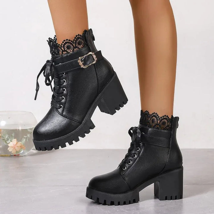 Black leather lace-up ankle boots with chunky heels and decorative gold buckle on model's feet