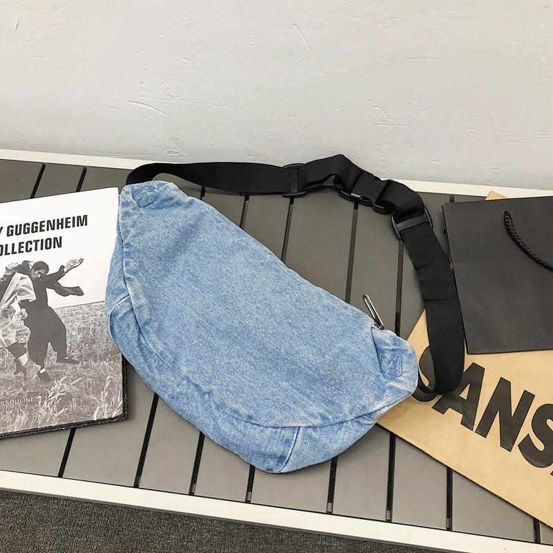 Light blue denim waist bag with adjustable black strap on gray surface with books and shopping bag