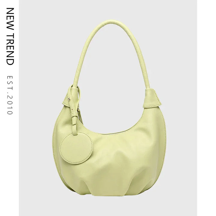 Light green leather shoulder hobo bag with round tag on gray background, new trend handbag