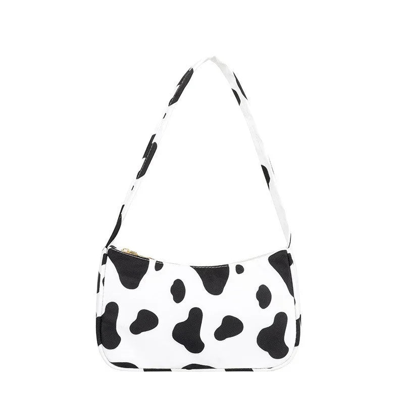 Stylish white handbag with black cow print pattern and matching shoulder strap on white background