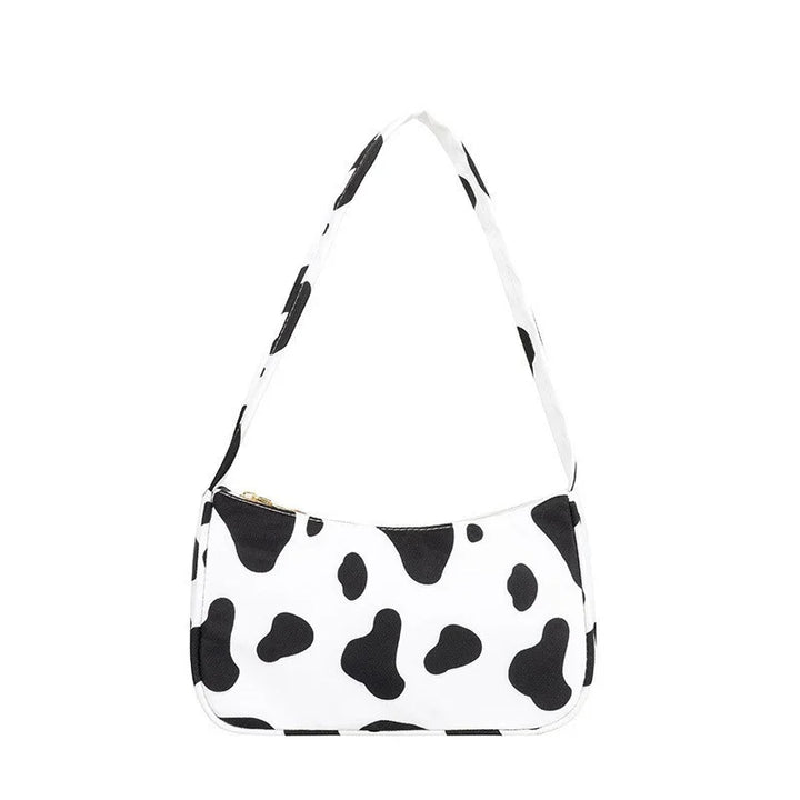 Stylish white handbag with black cow print pattern and matching shoulder strap on white background