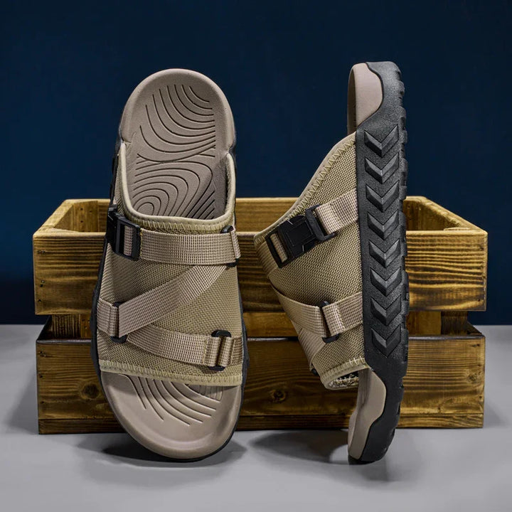 Beige outdoor sandals with adjustable straps and black textured soles displayed on a wooden crate