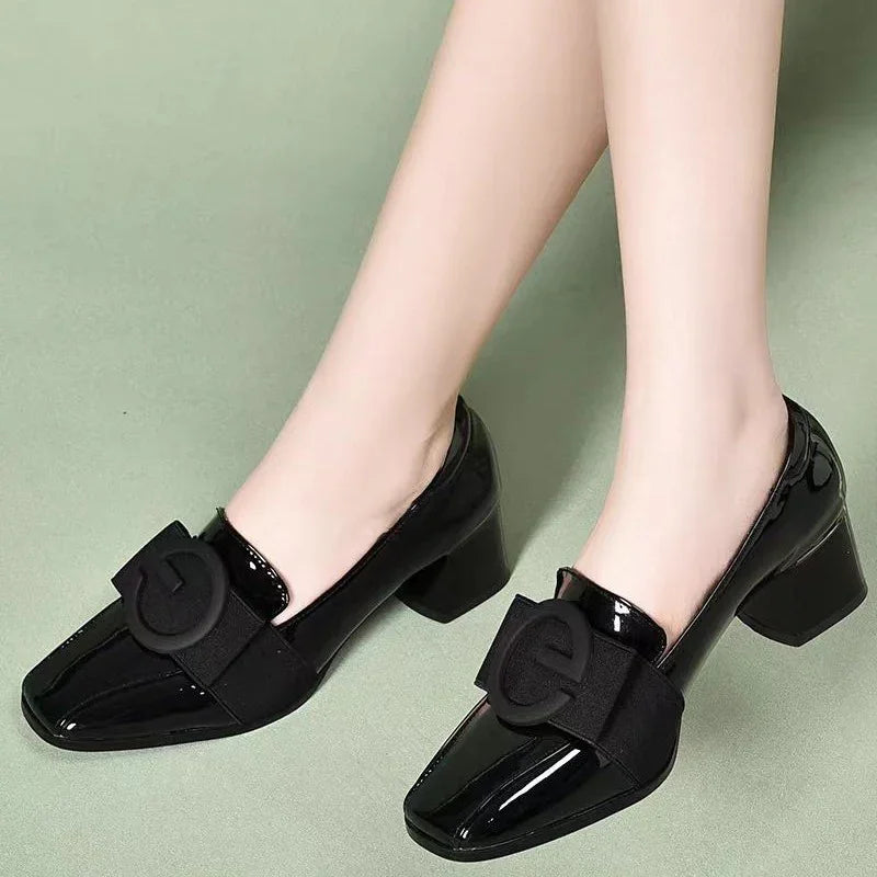 Black patent leather block heel shoes with large black buckle detail worn on feet