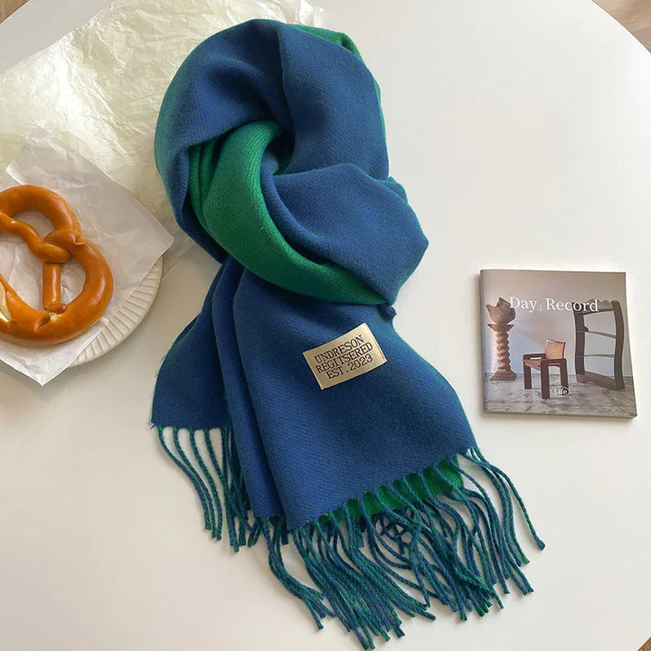 Blue and green fringed scarf with Undreson Registered Est. 2023 label on white table with pretzel and Day Record booklet