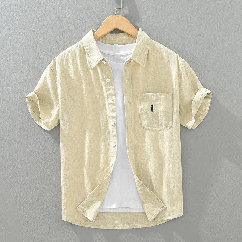 Beige short-sleeve button-up shirt with chest pocket layered over white t-shirt on wooden hanger