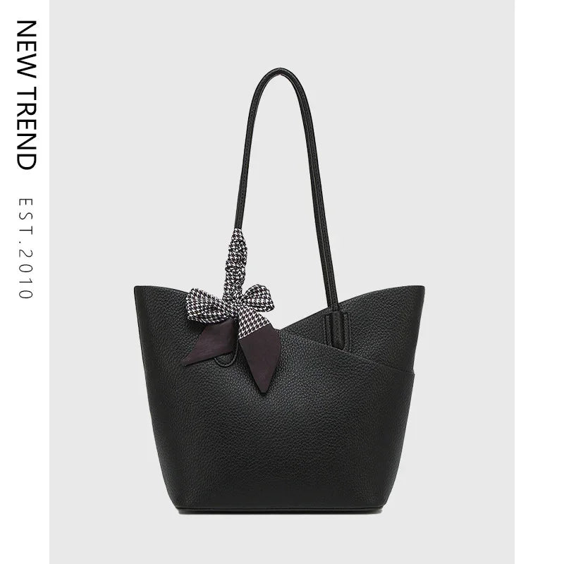 Black textured leather tote bag with long handles and black-and-white patterned bow accessory