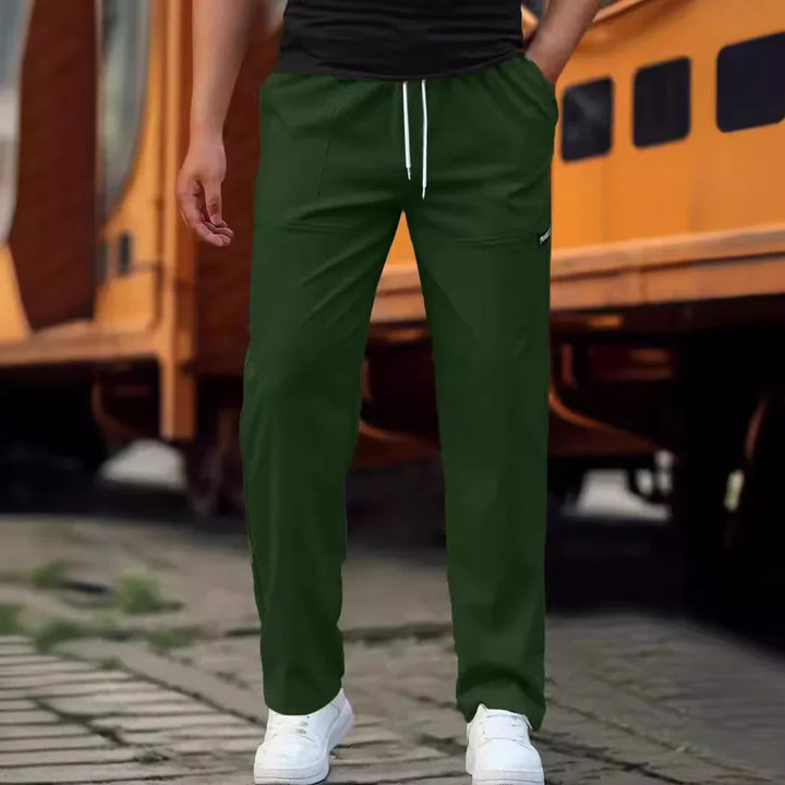 Man wearing dark green casual pants with white drawstring and white sneakers outdoors near yellow train