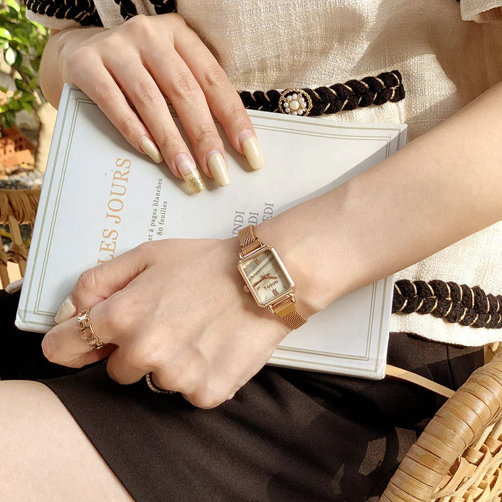Woman wearing rose gold mesh watch and rings holding a white book titled LES JOURS