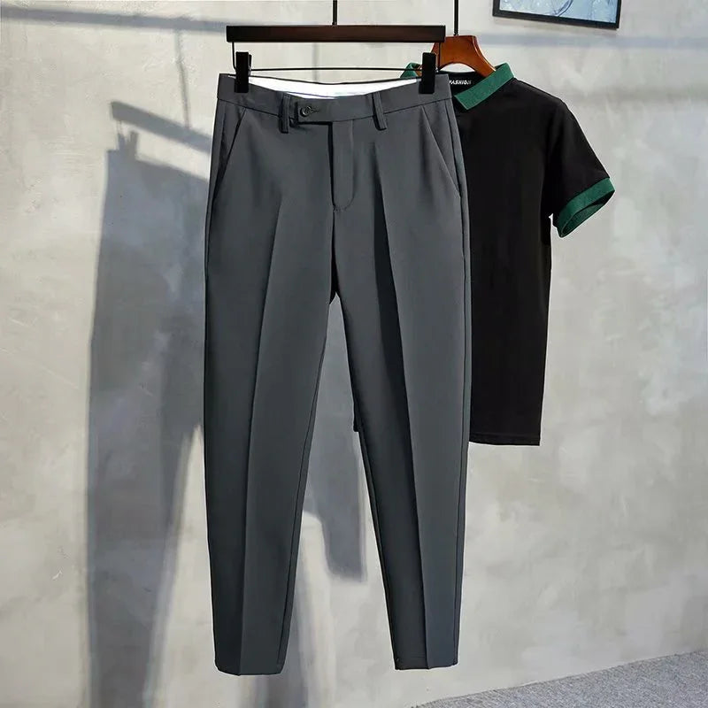 Gray tailored dress pants hanging on a wooden hanger with a black polo shirt featuring green collar and sleeve trim