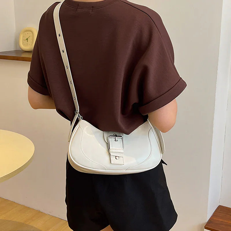 Woman wearing a brown t-shirt and black shorts with a white leather shoulder bag featuring a buckle strap