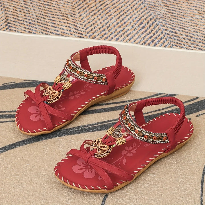 Pair of red women's sandals with floral and beaded decoration on patterned floor