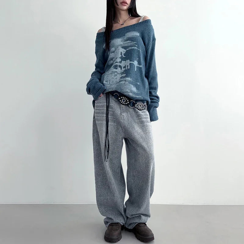 Woman wearing loose gray pants, blue off-shoulder sweater, decorative belt, and brown shoes against plain background