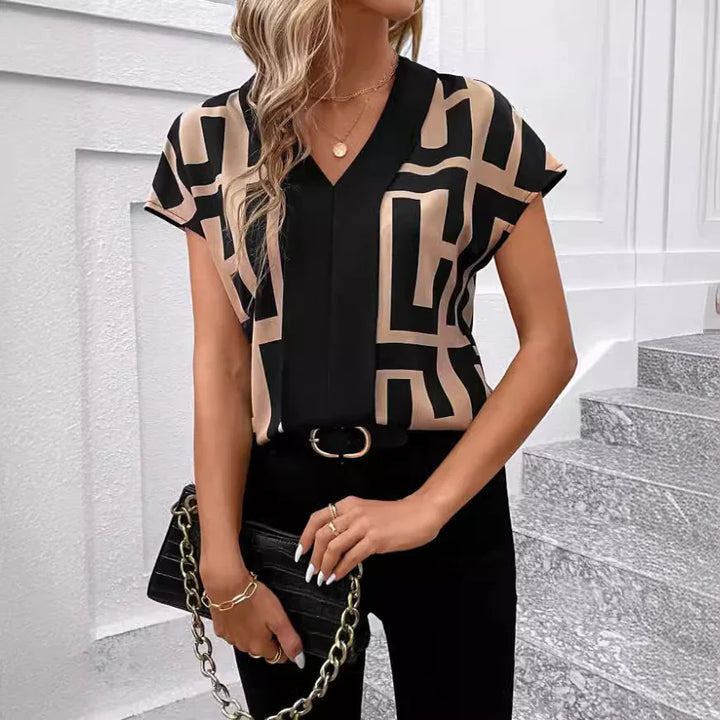 Woman wearing geometric black and beige short-sleeve blouse with black pants and gold accessories