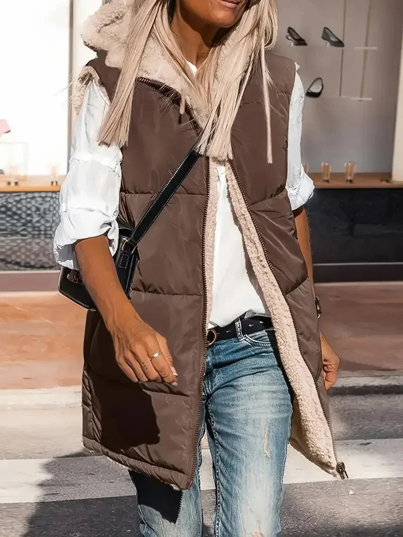 Woman wearing brown padded sleeveless vest with sherpa lining, white blouse, and blue jeans outdoors