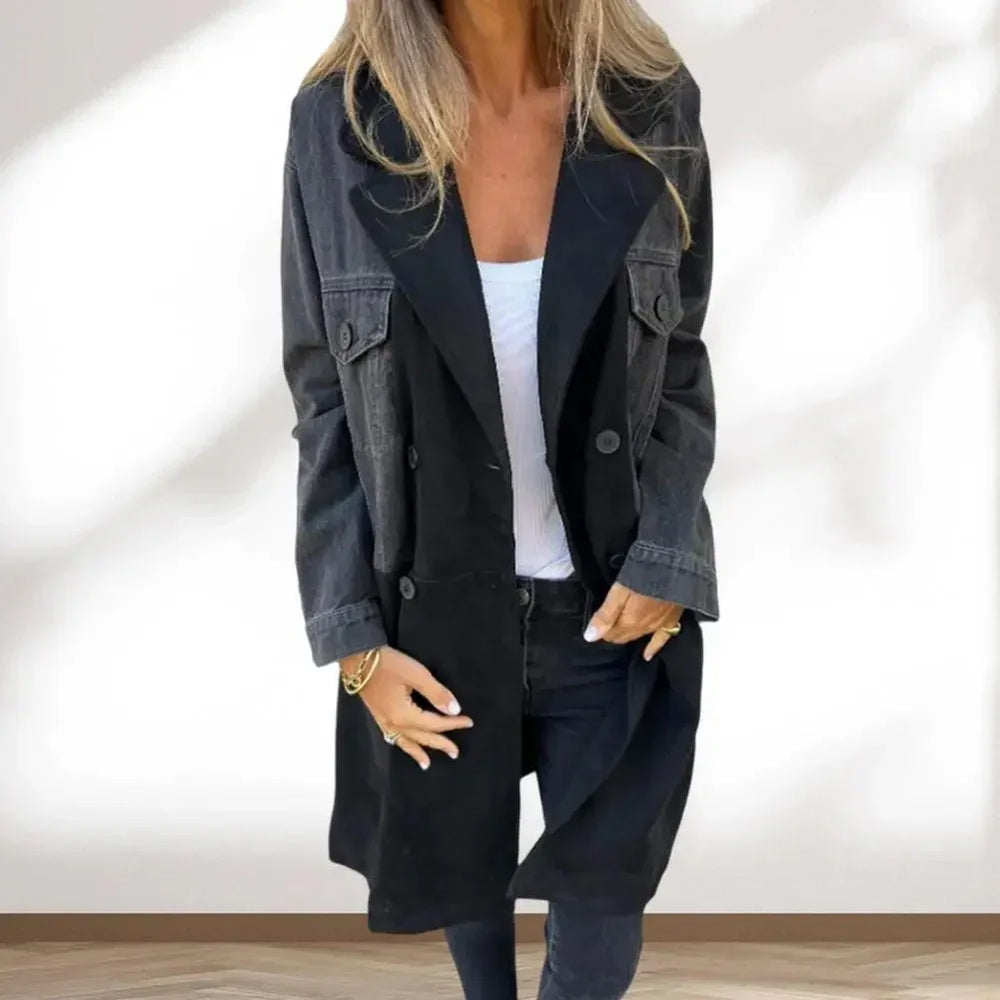 Woman wearing black buttoned trench coat over white top and black pants, standing indoors