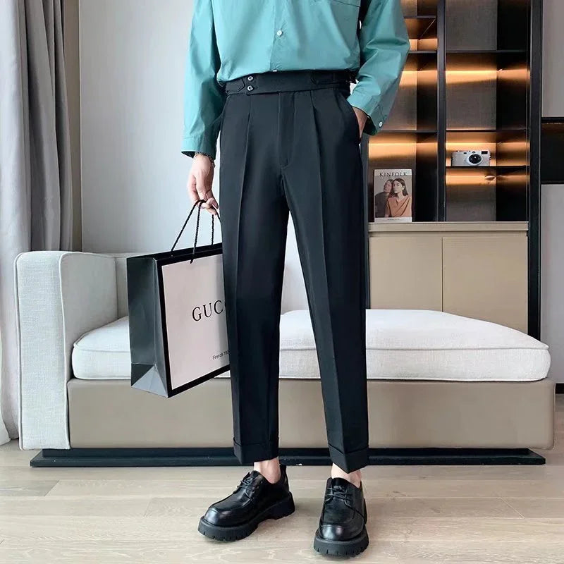 Man wearing black tailored trousers, turquoise shirt, black leather shoes, holding a Gucci shopping bag indoors
