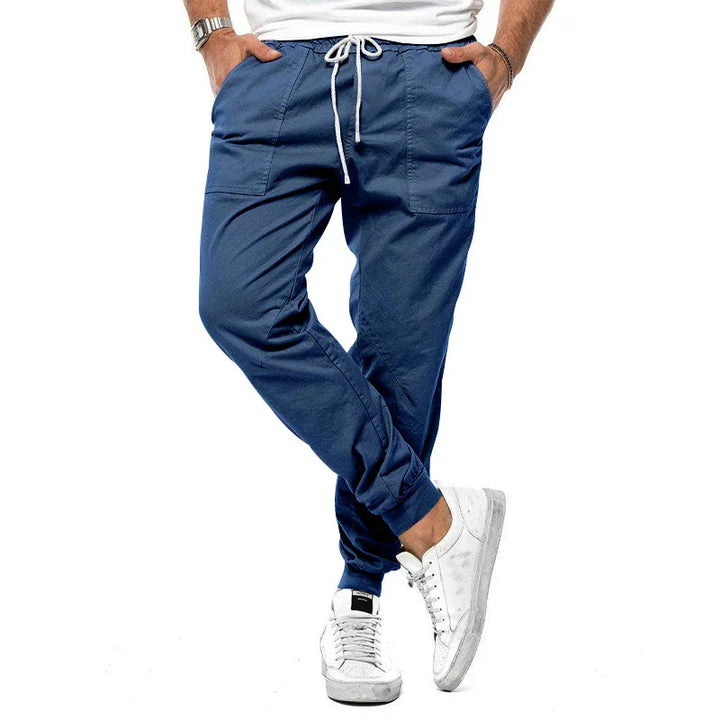 Man wearing navy blue jogger pants with white drawstring and white sneakers on white background