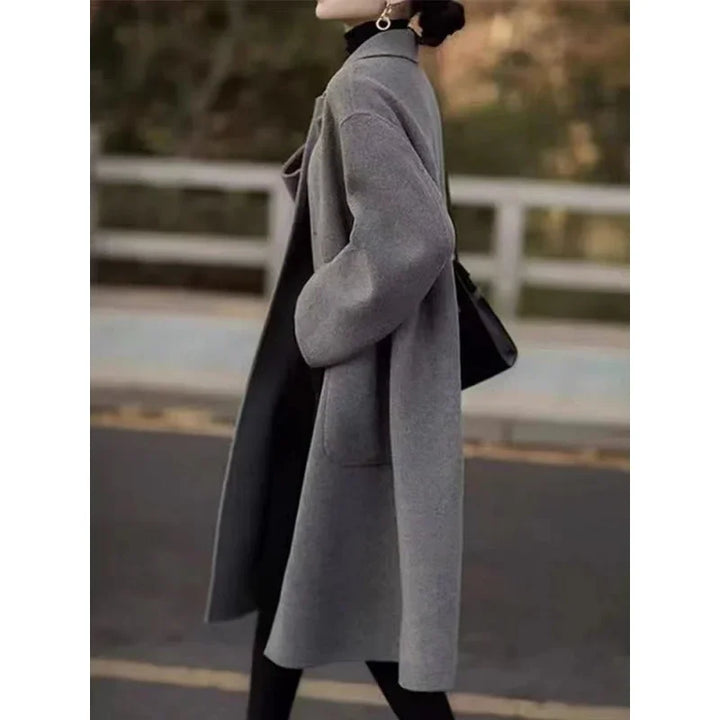 Woman wearing a stylish gray wool coat over black outfit walking outdoors with black handbag