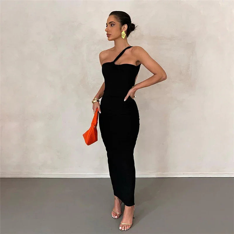 Woman in black one-shoulder dress with orange handbag and gold earrings on gray floor