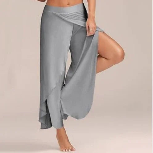 Woman wearing stylish gray wrap pants with wide legs, posed with one leg raised in studio