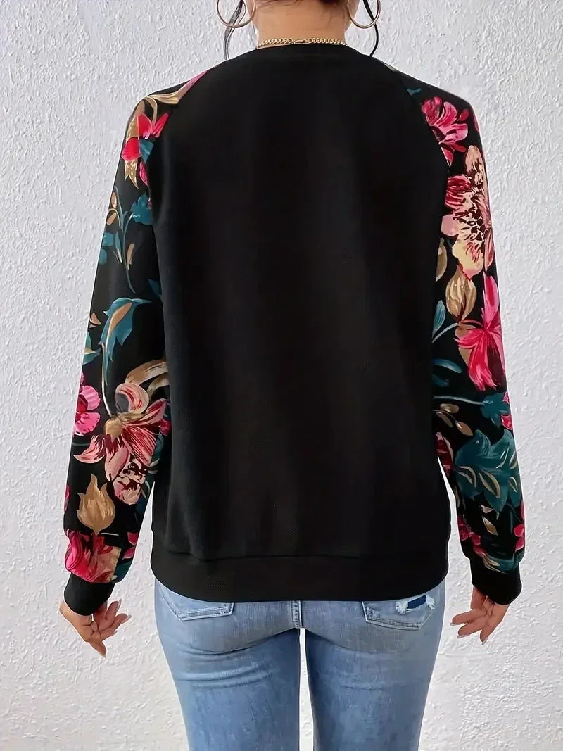 Back view of woman wearing black sweatshirt with colorful floral print sleeves and light blue jeans