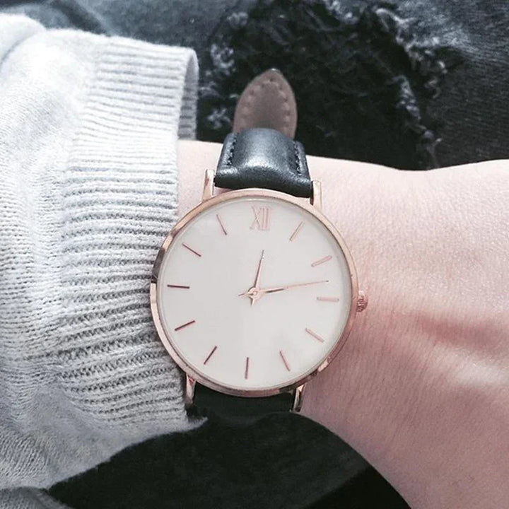 Minimalist wristwatch with white dial and black leather strap on wrist with gray sweater