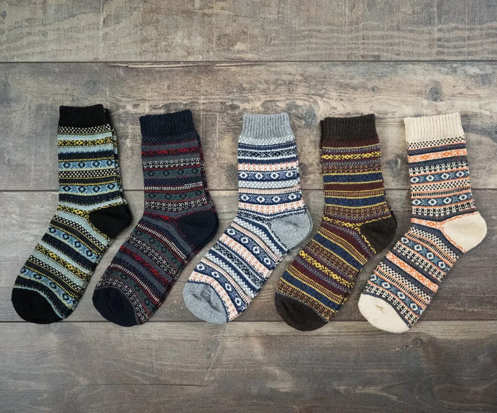 Five pairs of patterned woolen socks in various colors laid out on wooden floor