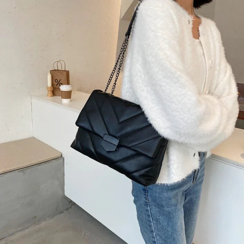 Woman wearing white fuzzy cardigan and blue jeans carrying black quilted leather shoulder bag with chain strap indoors