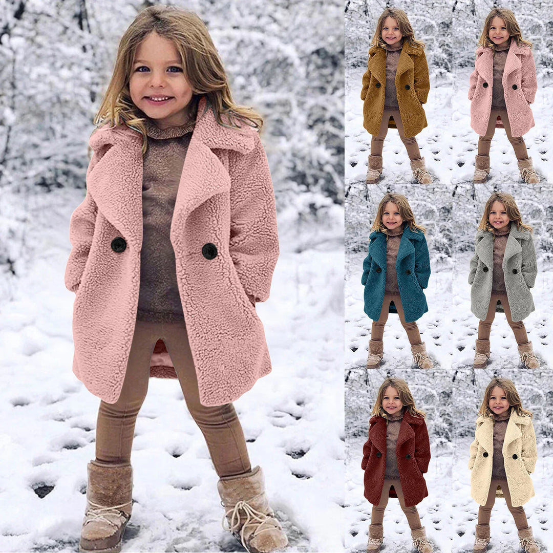 Smiling girl in tan pants and boots wearing pink, brown, blue, gray, red, and cream teddy coat in snowy forest