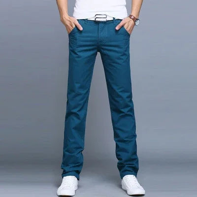 Man wearing slim fit blue casual pants with white belt and white sneakers against gray background