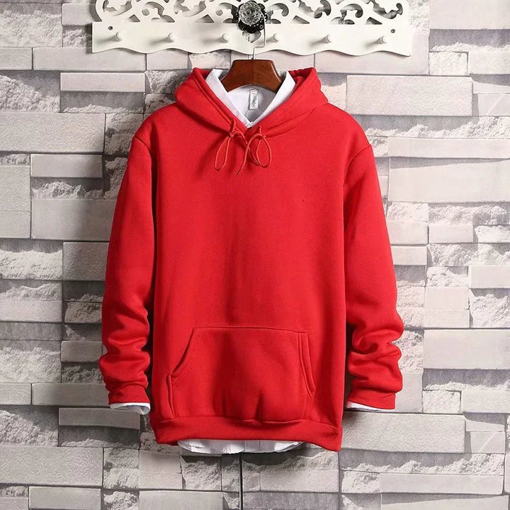 Red hoodie with front pocket hanging on decorative white wall hook against gray brick wall background