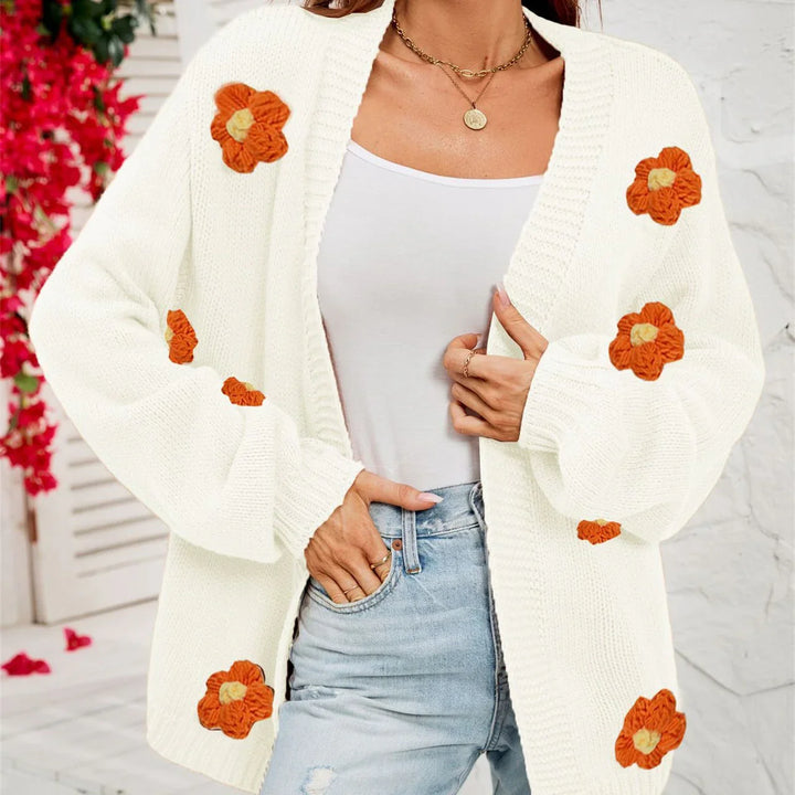 Woman wearing white knitted cardigan with orange flower appliques and light blue jeans
