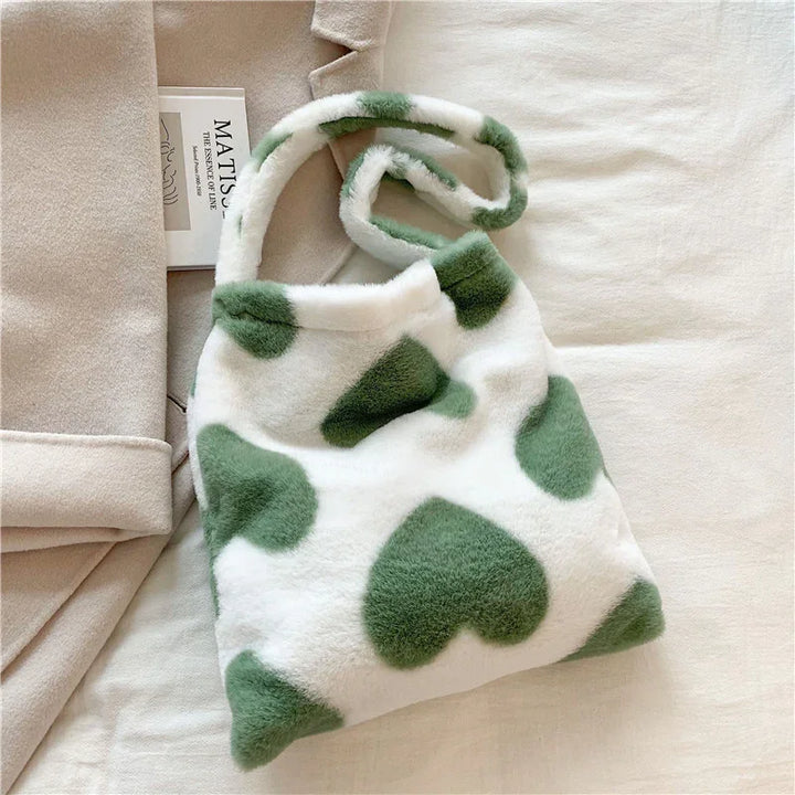 Soft white plush handbag with large green heart patterns on a beige fabric background