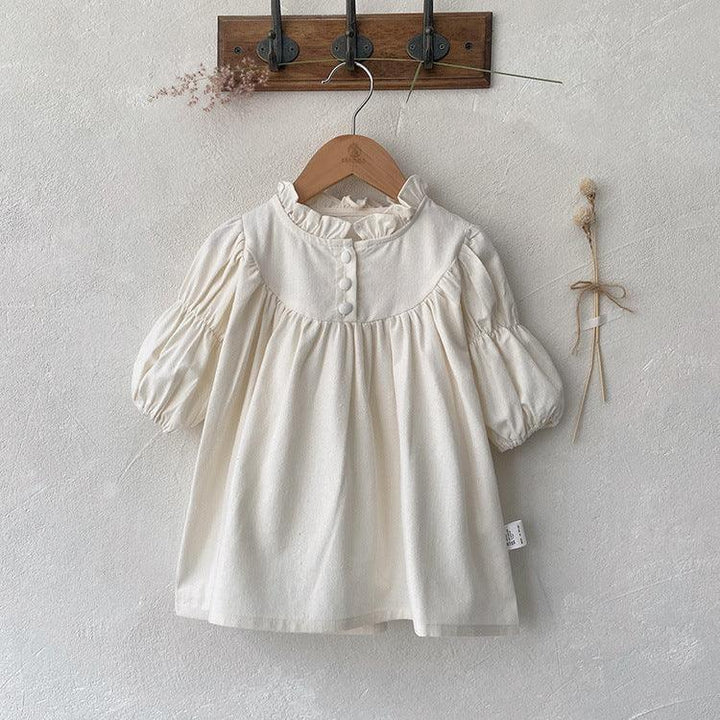 Cream-colored baby dress with ruffled collar and puffed sleeves hanging on wooden hanger
