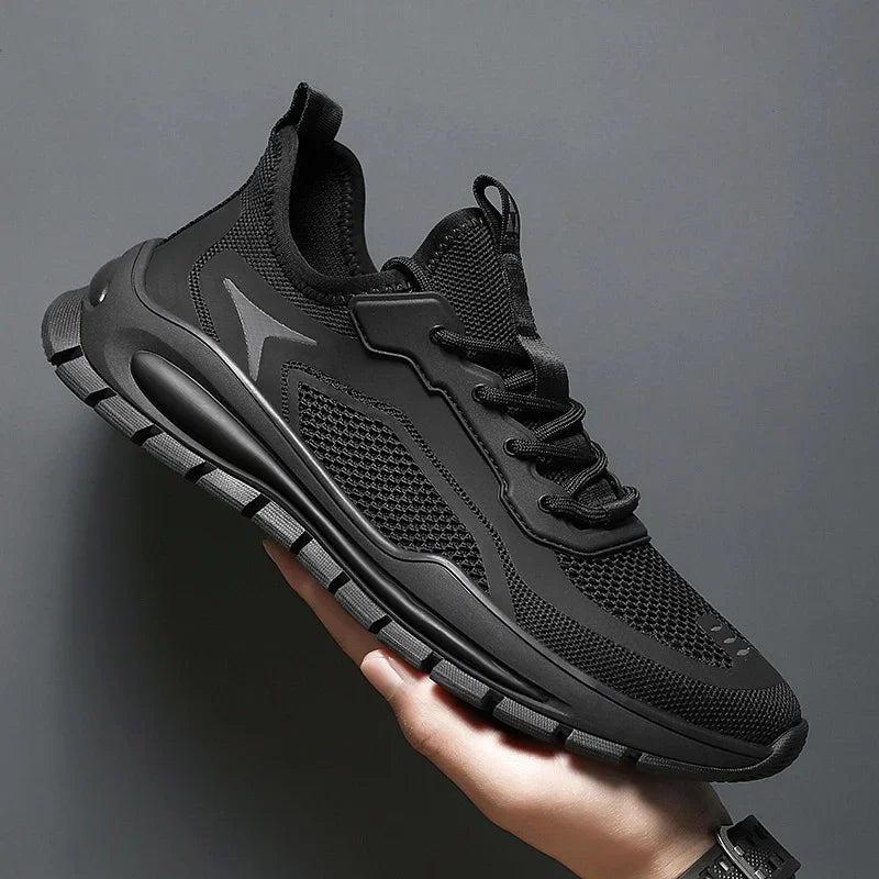 Hand holding a black mesh athletic sneaker with sturdy sole and lace-up design against a gray background